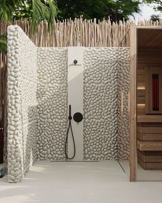 an outdoor shower with rocks and bamboo in the back ground, next to a tree