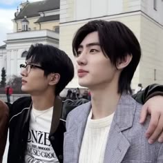 two young men standing next to each other in front of a building with people walking around