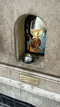 a glass of white wine sitting on top of a stone wall next to a plaque