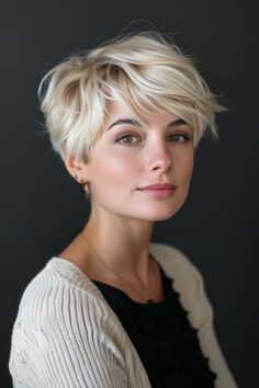 A person with short blonde hair and a subtle smile, wearing a white cardigan and black top against a dark background. Sleek Pixie, Bixie 90s Haircut Short, Straight Hair Pixie Haircut, Feminine Pixie Cut, Pixie Grow Out Style, Pixie Haircut With Bangs, Blonde Pixie Cut, Modern Pixie Haircut, 90s Pixie Cut