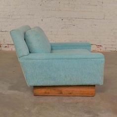 a light blue couch sitting on top of a wooden stand in front of a white brick wall