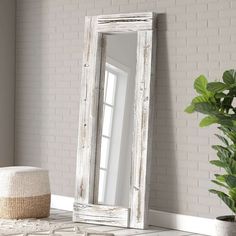 a white wooden mirror sitting on top of a table next to a potted plant