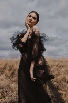 a woman standing in a field with her hand on her face and looking off to the side