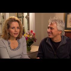 a man and woman sitting next to each other in front of a table with flowers on it