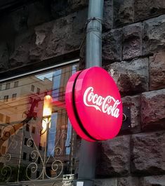 a coca - cola sign hanging from the side of a building next to a street light