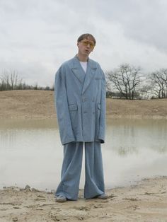 a man standing in front of a body of water wearing a blue suit and sunglasses