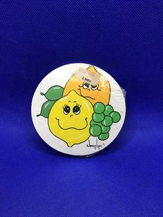 a button with two lemons and grapes on it, sitting on a blue background