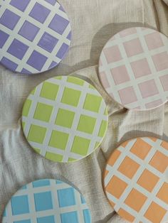 four different colored coasters sitting on top of a white cloth covered table with checkered design