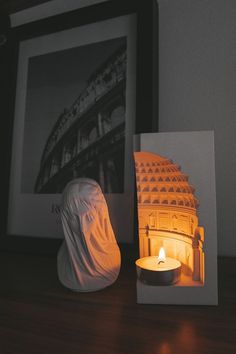 a lit candle is sitting next to a paper sculpture on a table in front of a framed photograph