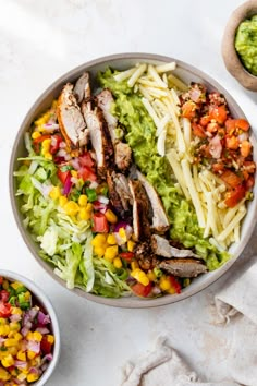 a salad with chicken, lettuce and corn in a bowl next to two bowls