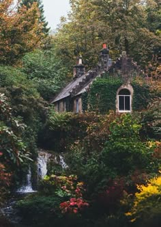 the house is surrounded by trees and flowers with a waterfall coming out of the window