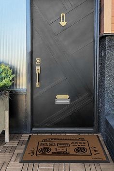 a black door with a brown mat on the floor and potted plants in front