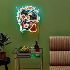 a neon sign is on the wall above a small table with fruit and a bottle