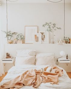 an unmade bed in a white bedroom with plants on the wall and pictures above it