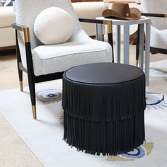 a living room with two chairs and a table in front of the chair is a round ottoman that has fringed tassels on it