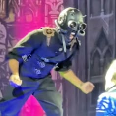 a man in a diving suit and gas mask running on stage with another person behind him