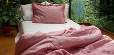 a bed covered with pink sheets and pillows in front of a window overlooking the forest