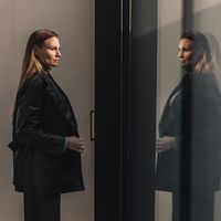 two women standing in front of a glass door looking at each other and talking to each other