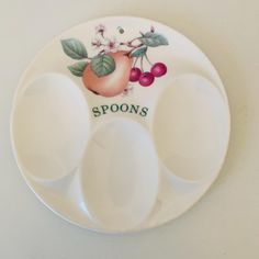 three spoons and two plates with fruit painted on the sides, sitting on a white surface