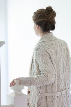 a woman in a white coat is standing next to a railing and looking out the window