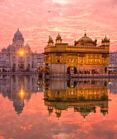 the golden temple in amritra india is reflected in the still water at sunset