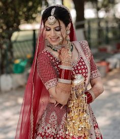 a woman in a red and gold bridal outfit with jewelry on her hands, smiling at the camera