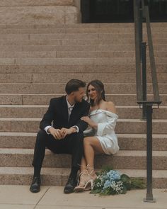 a man and woman sitting on steps next to each other with flowers in front of them