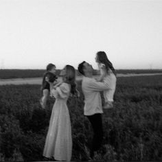 a man and woman kissing while holding two children in a field with other people behind them