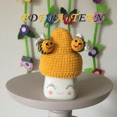 there is a crocheted hat on top of a table with flowers in the background