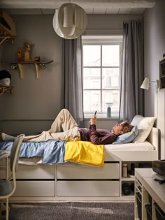 a man laying on top of a bed in a bedroom next to a desk and window