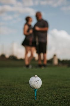 a golf ball sitting on top of a green grass covered field next to a couple