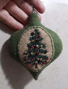 a hand holding a green ornament with a christmas tree on it's side