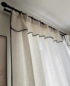 an open window with white curtains hanging from the side and black trimmings on the bottom