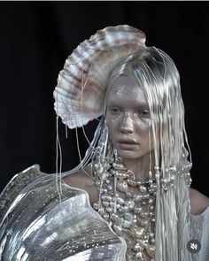 a woman with white makeup and silver hair wearing a large shell on top of her head