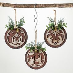 three wooden ornaments hanging from a tree branch with green leaves on them, depicting the birth of jesus