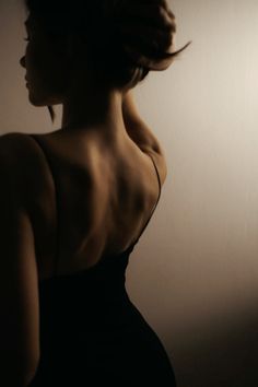 a woman in a black dress with her back turned to the camera, looking off into the distance