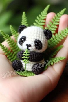 a small stuffed panda bear sitting on top of a green leafy plant in someone's hand