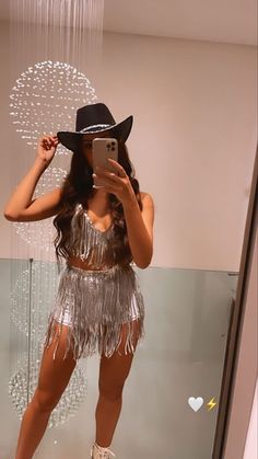 a woman taking a selfie in front of a mirror wearing a hat and fringe skirt