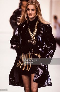 a woman is walking down the runway wearing a black outfit with gold chains on it