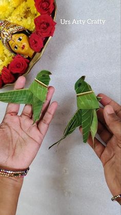 two hands are holding small green leaves in front of a flower arrangement with buddha face on it