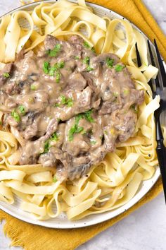 a white plate topped with pasta covered in gravy next to two black forks