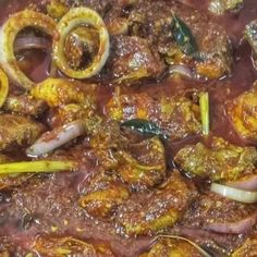 meat and vegetables are being cooked in a large pot with red sauce on the side