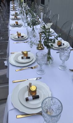 a long table set with white plates and silverware, gold place settings and flowers