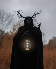 a person dressed as a witch holding a lantern in front of their face and wearing a black cloak