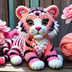 a crocheted tiger sitting on top of a wooden table next to pink flowers