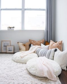 a living room with white rugs and pillows on the floor next to a window