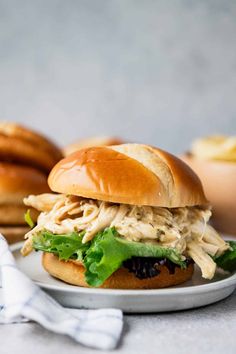 a chicken sandwich with lettuce and black olives on a plate next to some bread rolls