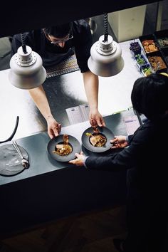 two people standing at a counter preparing food