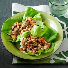 lettuce wraps filled with meat and vegetables on a green plate next to a glass of water