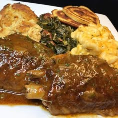 a white plate topped with meat covered in gravy next to potatoes and spinach